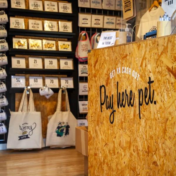 Geordie Gifts in Grainger Market. The shop counter has the message "Pay here pet". In the background are a range of cards and tote bags with phrases in the Geordie dialect.